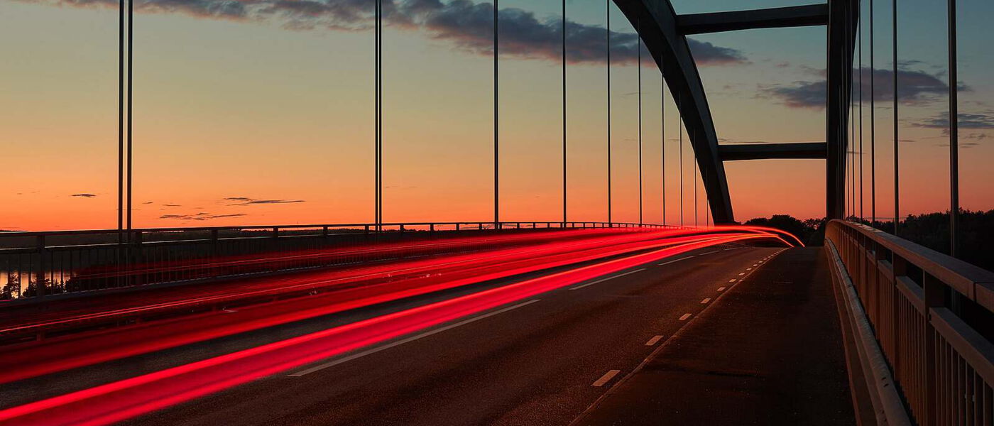 INQA - Symbol: verwischende rote Rücklicher von Autos auf einer Brücke