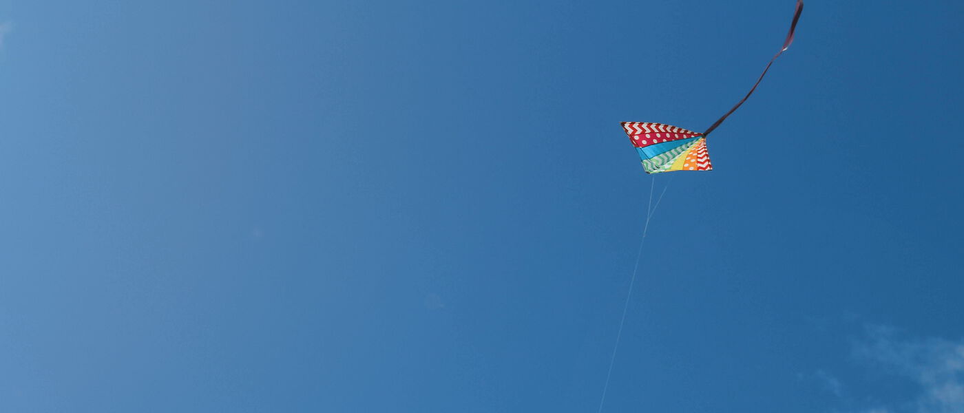 Ein bunter Kinderdrachen in einem blauen Himmel mit wenigen weißen Wolken